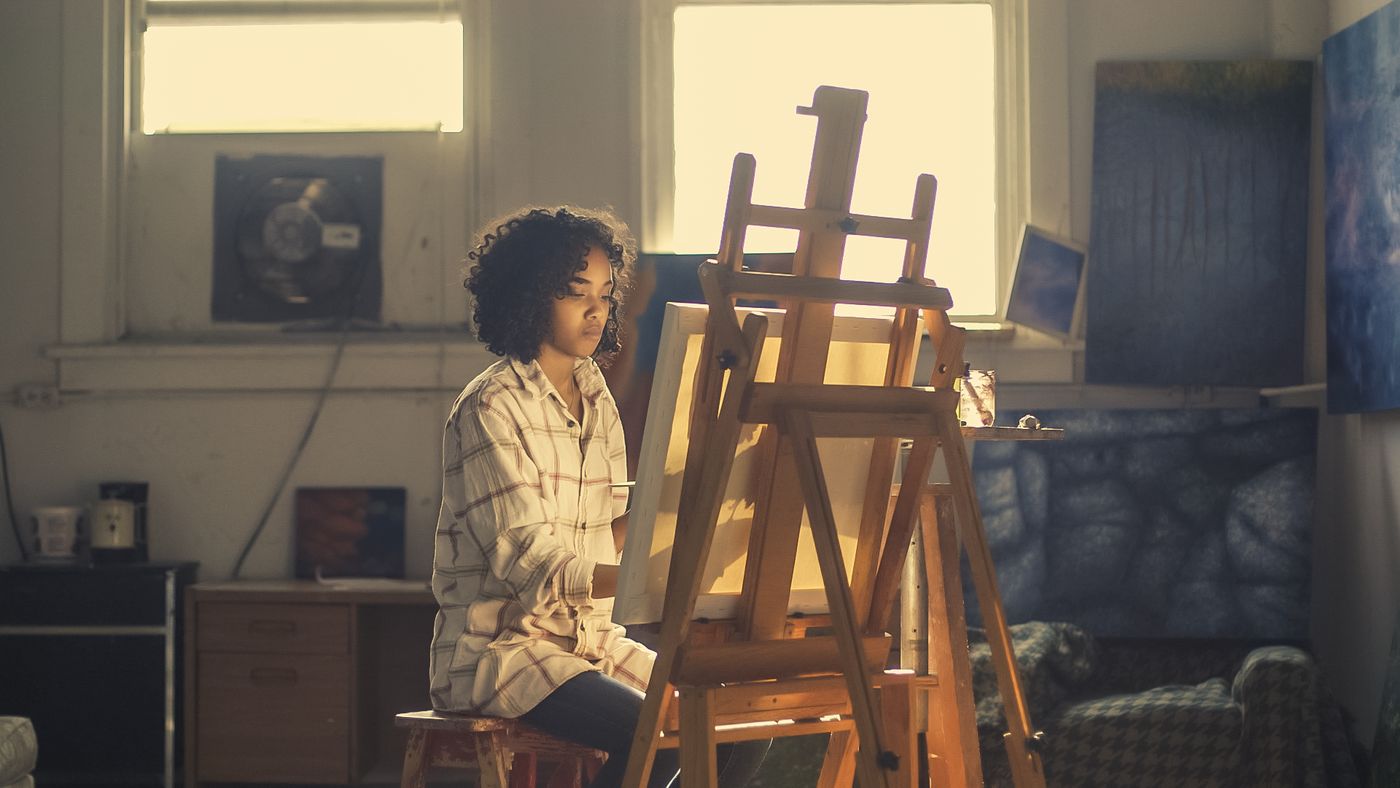 An artist painting at an easel in a bright studio